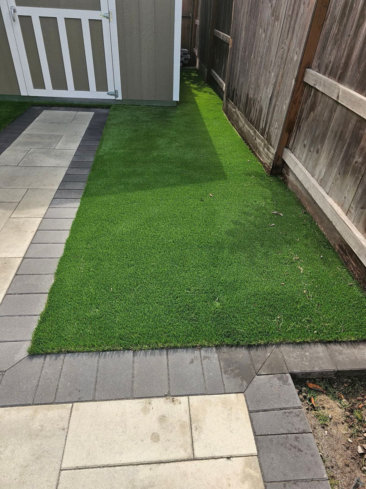 narrow strip of artificial turf installed along a side yard between a paver walkway and wood fence in Stockton, California