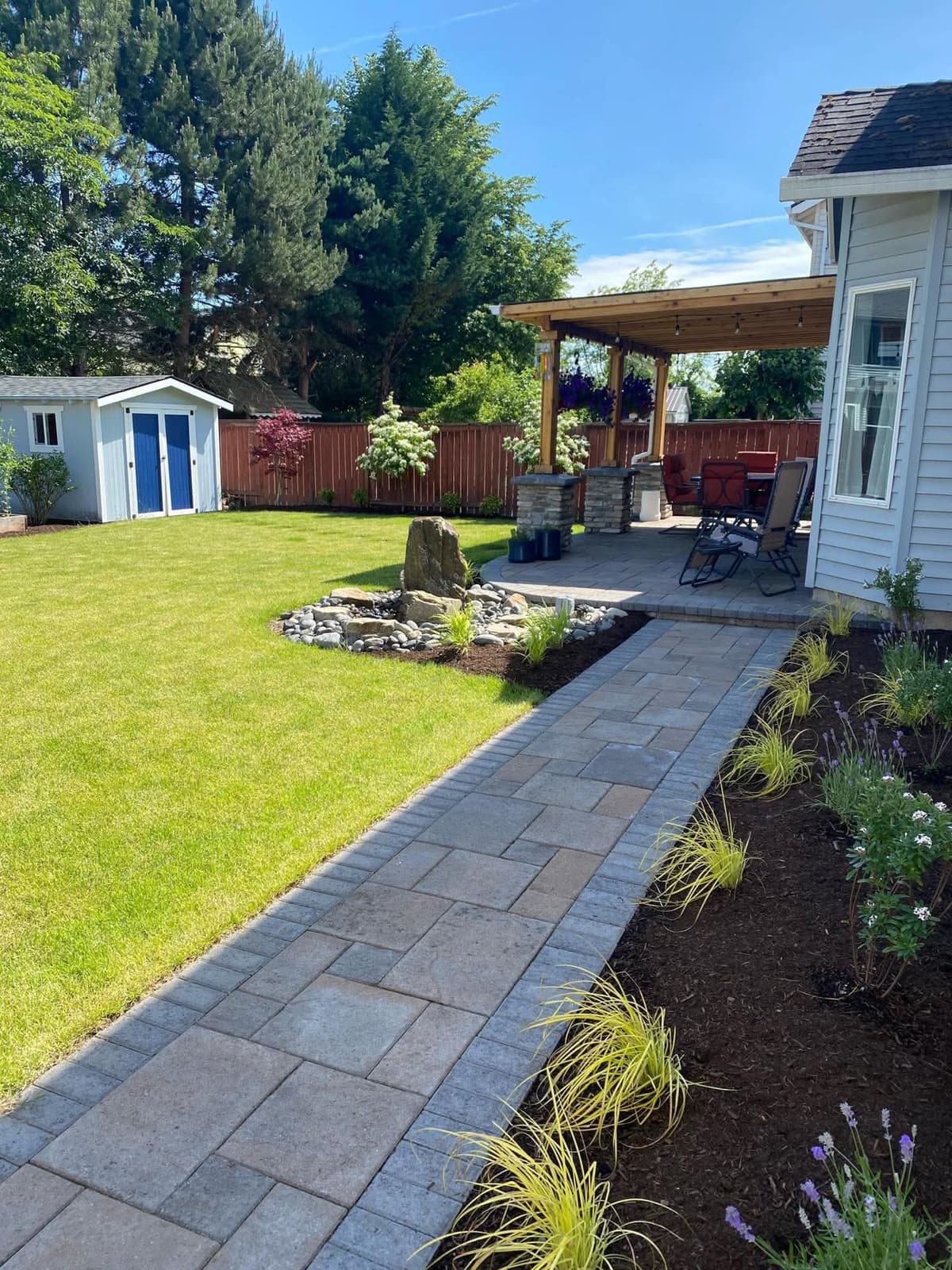 manicured backyard lawn with a paver walkway leading to a pergola-covered patio and boulder water feature in Stockton, California