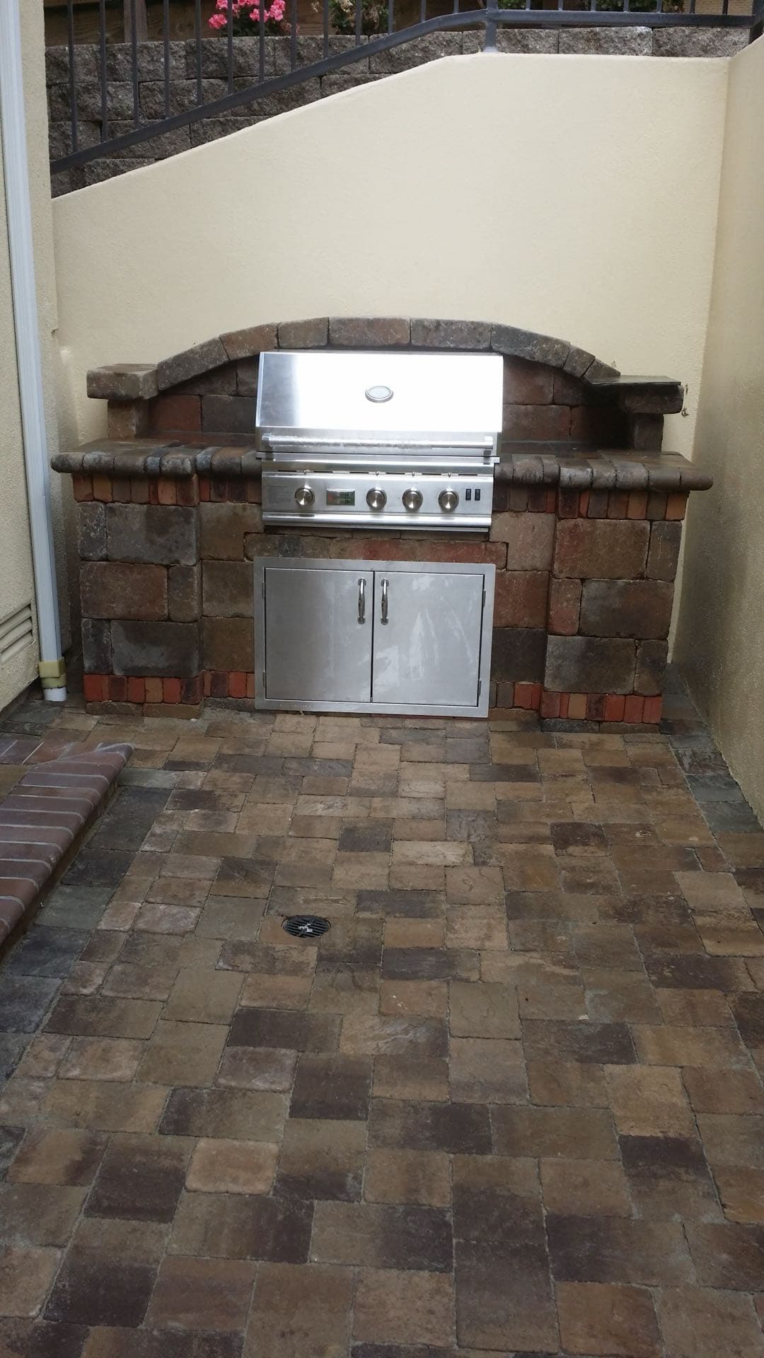 built-in stainless steel BBQ grill with a stacked stone surround and paver countertop in a backyard corner in Stockton, California
