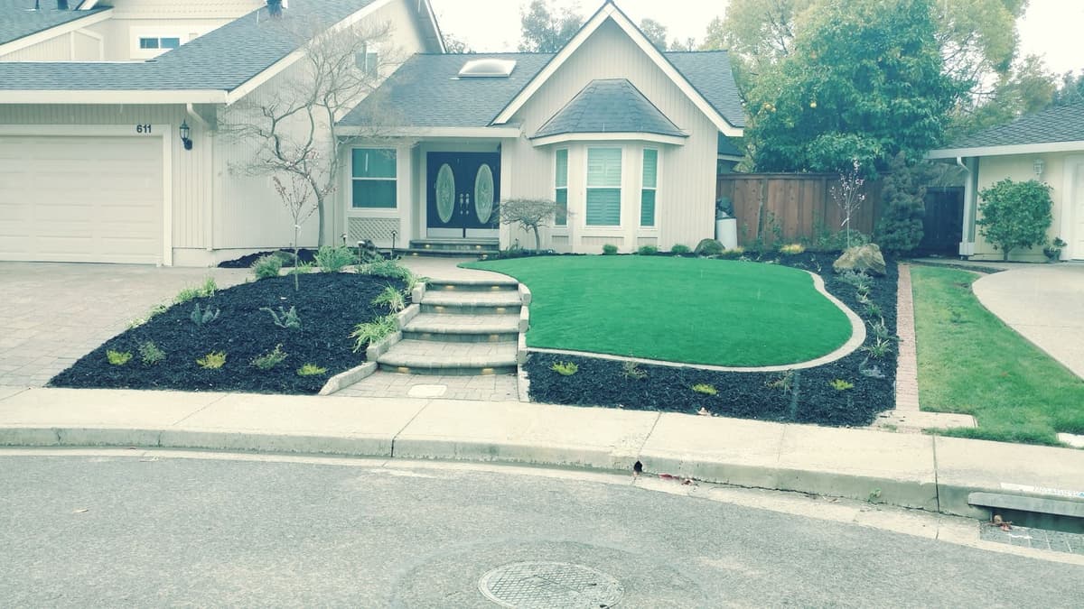 front yard with a curved synthetic turf lawn, mulch planting beds, and paver entry steps in Stockton, California