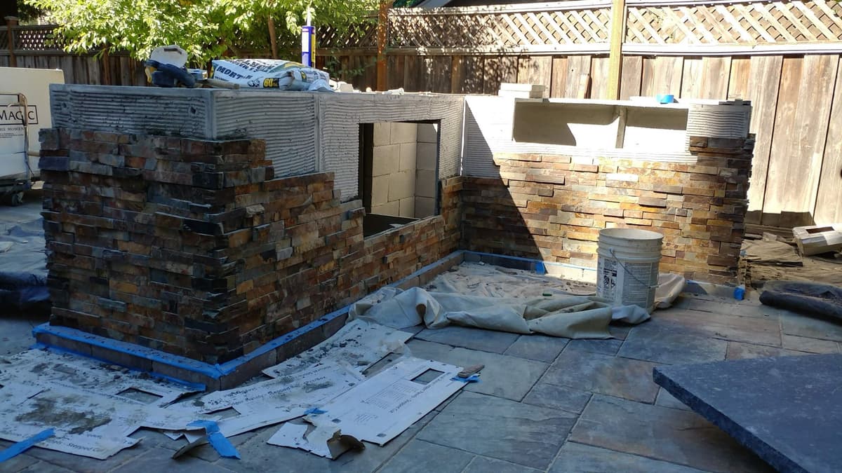 outdoor kitchen structure under construction with stacked stone veneer being applied to the block walls in Stockton, California