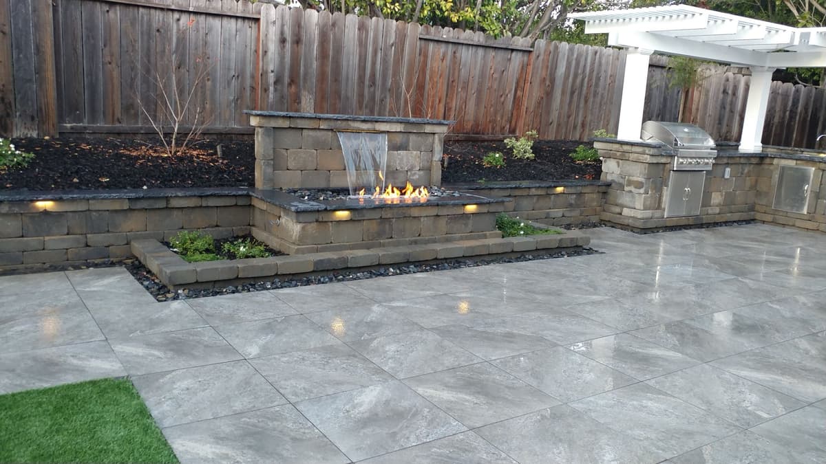 backyard paver patio with a fire and water feature wall, raised planters, and an outdoor kitchen under a pergola in Stockton, California