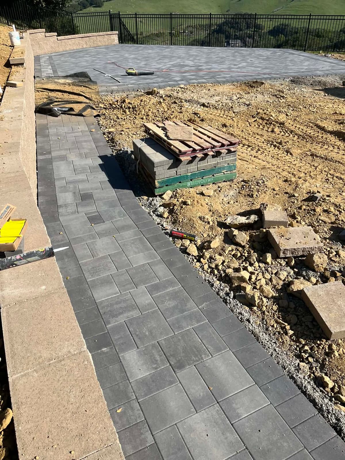 paver patio installation in progress with a scenic hillside view and wrought iron fence in Stockton, California