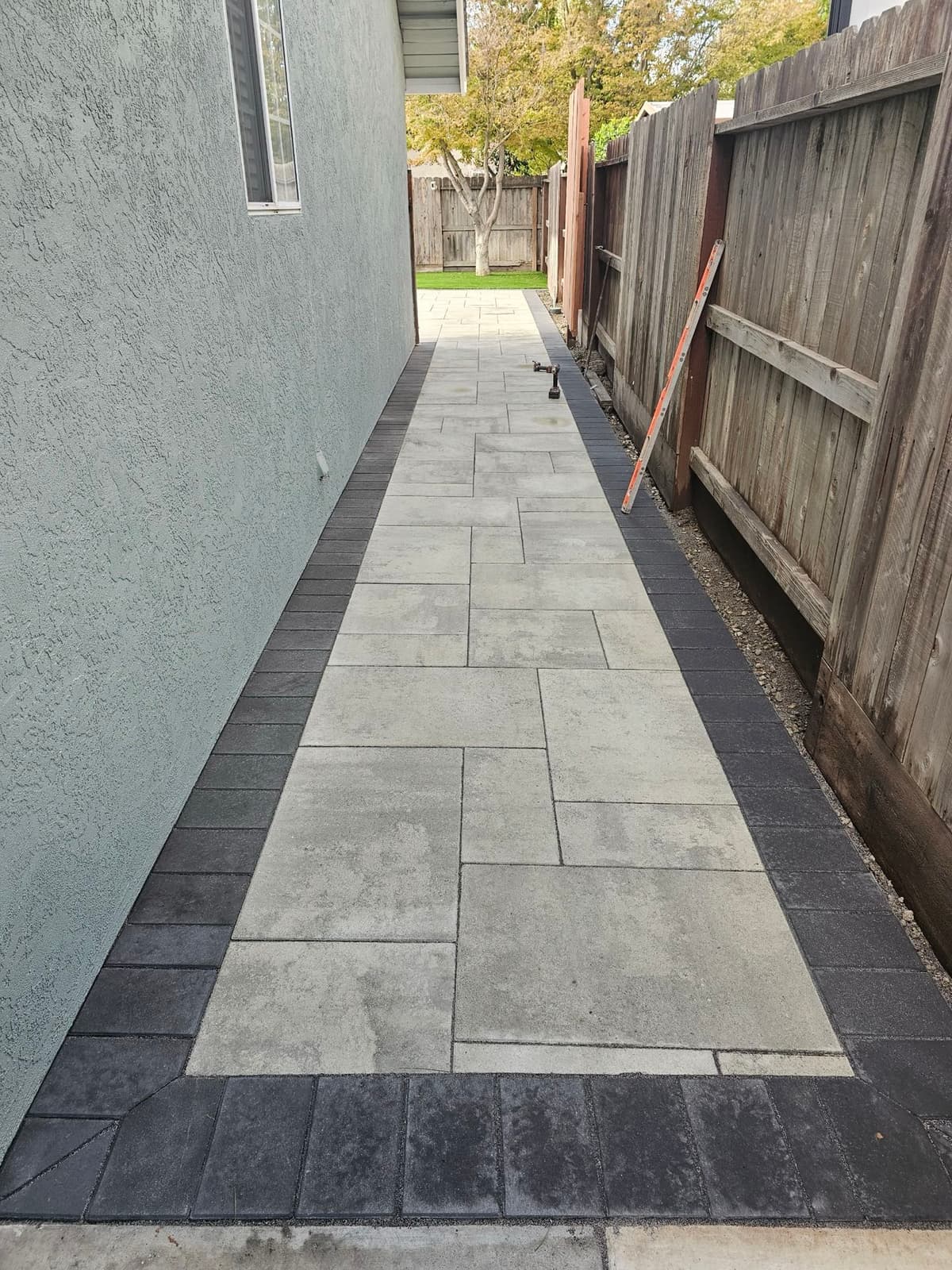narrow side-yard paver walkway with a charcoal paver border leading to a backyard patio in Stockton, California