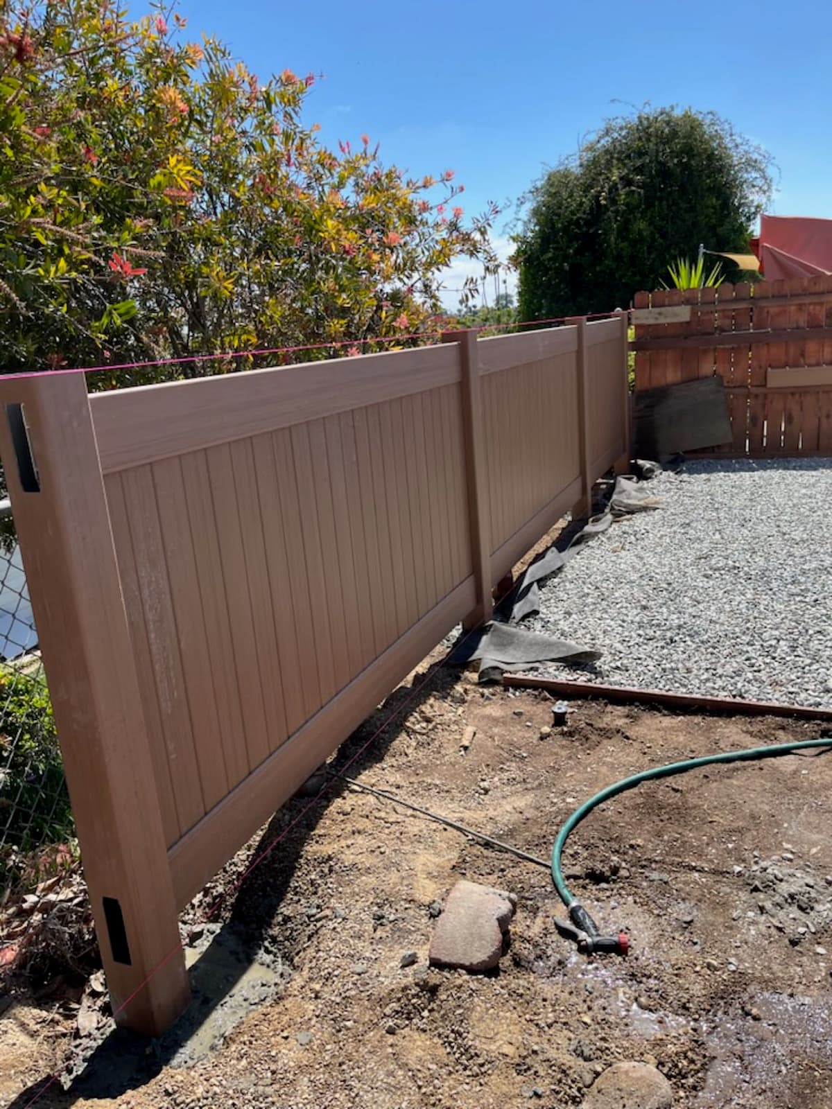 vinyl privacy fence panel being installed along a gravel side yard in Stockton, California